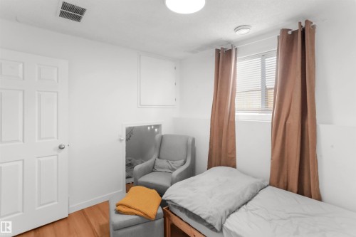 White paneled door, wood-finish flooring, white walls, window with blinds, and ceiling-mounted light fixture - 679 Kananaskis Drive, Devon, AB - Indoor Photo Showing Bedroom
