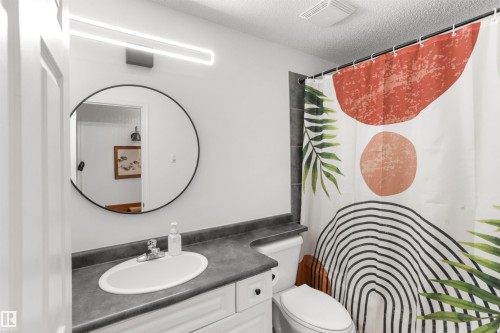 Bathroom featuring a circular mirror, contemporary vanity lighting, white single-basin sink, and a dark countertop - 679 Kananaskis Drive, Devon, AB - Indoor Photo Showing Bathroom