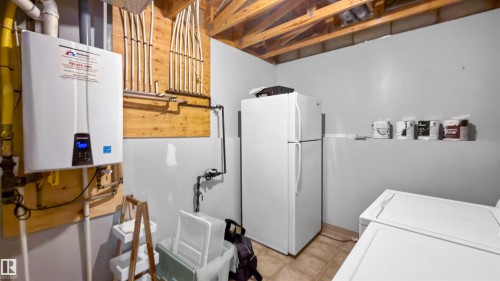 Utility area featuring a wall-mounted tankless water heater, exposed wood ceiling joists, and light gray painted walls - 679 Kananaskis Drive, Devon, AB - Indoor Photo Showing Laundry Room