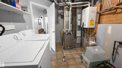 Utility area featuring tile flooring, wall-mounted shelving, and a tankless water heater - 679 Kananaskis Drive, Devon, AB - Indoor Photo Showing Laundry Room