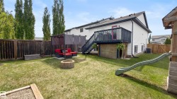 Expansive backyard featuring a raised wood deck with staircase, white siding exterior, and a stone-clad foundation - 