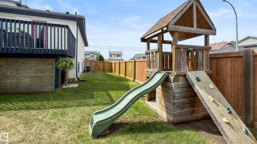 Expansive backyard featuring a manicured lawn, full wood fencing, a dedicated outdoor play structure with slide, and a raised exterior deck - 679 Kananaskis Drive, Devon, AB - Outdoor