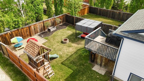 Expansive backyard featuring a manicured lawn, full privacy fencing, an elevated wooden deck with railing, a built-in fire pit, and mature perimeter landscaping - 679 Kananaskis Drive, Devon, AB - Outdoor With Deck Patio Veranda