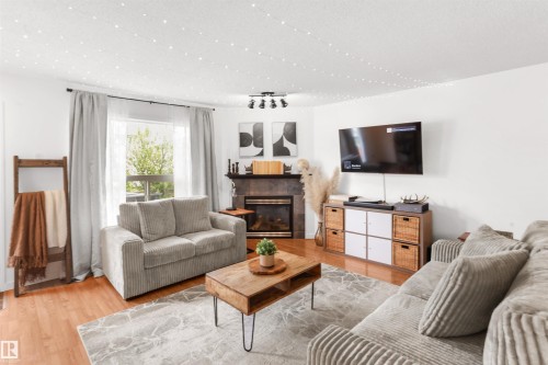 Living area featuring wood-finish flooring, a contemporary fireplace with a stone surround, and a large window - 679 Kananaskis Drive, Devon, AB - Indoor Photo Showing Living Room With Fireplace