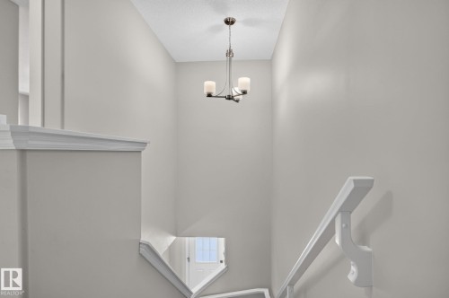 Stairwell featuring a bronze-finish chandelier with frosted glass shades, white painted handrails, and crown molding accents - 319 Desrochers Boulevard Sw, Edmonton, AB - Indoor Photo Showing Other Room