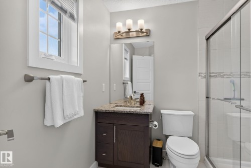 Bathroom featuring a dark wood-finish vanity with a speckled countertop, a toilet, and a glass-enclosed shower with tile surround and decorative accent band - 319 Desrochers Boulevard Sw, Edmonton, AB - Indoor Photo Showing Bathroom