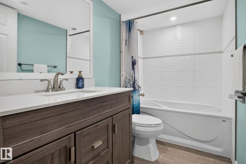 Bathroom featuring a wood-finish vanity with a white countertop and undermount sink, brushed nickel faucet, and a large wall mirror - 319 Desrochers Boulevard Sw, Edmonton, AB - Indoor Photo Showing Bathroom