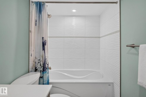 Deep soaking tub with textured white tile surround, recessed lighting, and a brushed nickel showerhead - 319 Desrochers Boulevard Sw, Edmonton, AB - Indoor Photo Showing Bathroom