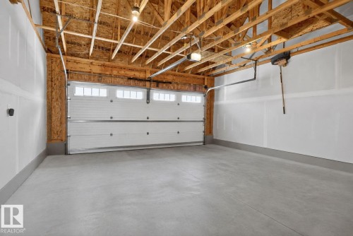 Spacious two-car garage featuring a concrete floor, exposed wood ceiling joists, and a white paneled garage door with upper window inserts - 319 Desrochers Boulevard Sw, Edmonton, AB - Indoor Photo Showing Garage