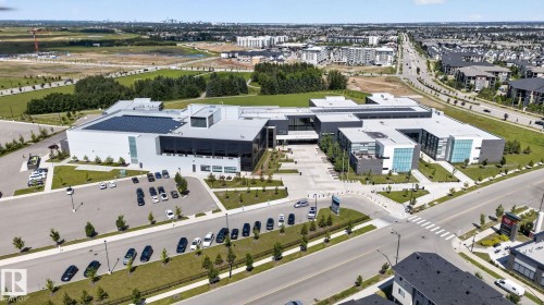 Modern institutional building featuring a multi-wing design, extensive rooftop solar panel array, structured parking areas, landscaped grounds, and a comprehensive hardscaped entrance plaza - 319 Desrochers Boulevard Sw, Edmonton, AB - Outdoor With View