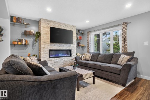 Living area featuring a floor-to-ceiling stacked stone fireplace with an integrated linear electric fireplace - 319 Desrochers Boulevard Sw, Edmonton, AB - Indoor Photo Showing Living Room With Fireplace