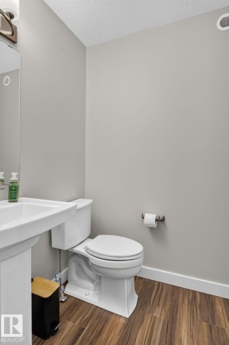 Pedestal sink with a wall-mounted mirror, white toilet, and wood-finish flooring - 319 Desrochers Boulevard Sw, Edmonton, AB - Indoor Photo Showing Bathroom