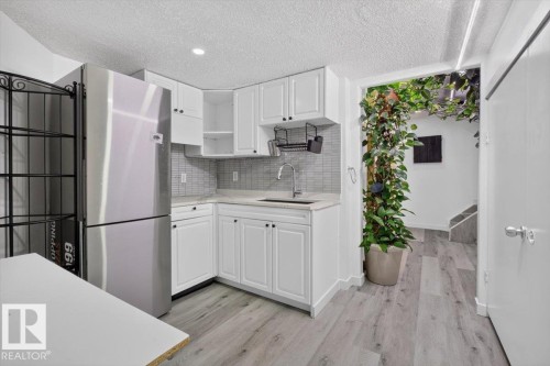 Modern kitchen featuring white cabinetry, a stainless steel refrigerator, and wood-finish flooring - #18 345 Kirkness Rd Nw, Edmonton, AB - Indoor Photo Showing Kitchen