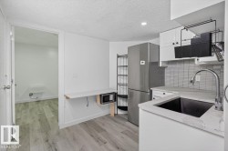Compact kitchen area featuring wood-finish flooring, white cabinetry, a stainless steel refrigerator, and a dark undermount sink with a gooseneck faucet - 