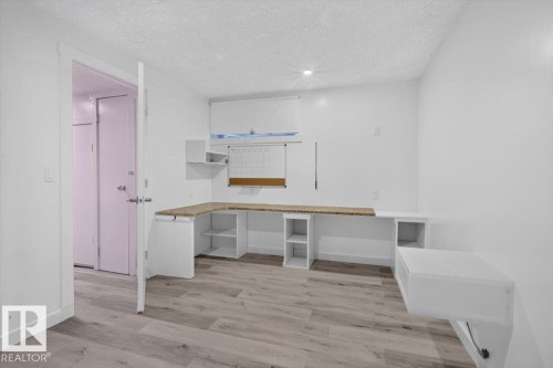 Built-in L-shaped desk with a light-toned countertop, integrated shelving, and wood-finish flooring - #18 345 Kirkness Rd Nw, Edmonton, AB - Indoor Photo Showing Other Room