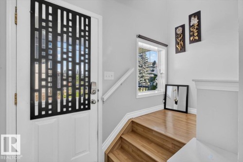 Entryway with a white door featuring a decorative black metal screen, wood-finish stairs, and a large window providing natural light - #18 345 Kirkness Rd Nw, Edmonton, AB - Indoor Photo Showing Other Room