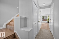 Entryway featuring a wood-finish staircase with white trim, a storage niche, and a tiled hallway - 