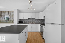 Kitchen featuring a spacious island with a dark countertop, white cabinetry with contemporary hardware, light wood-finish flooring, a mosaic tile backsplash, and track lighting - 