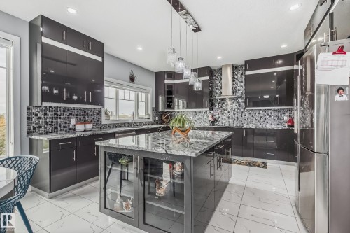 Kitchen featuring sleek dark cabinetry, a central island with a stone-finish countertop, a mosaic tile backsplash, recessed lighting, and a stainless steel refrigerator - 4104 8 Street Nw, Edmonton, AB - Indoor Photo Showing Kitchen With Upgraded Kitchen