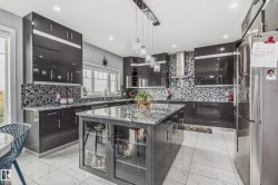 Kitchen featuring sleek dark cabinetry, a central island with a stone-finish countertop, a mosaic tile backsplash, recessed lighting, and a stainless steel refrigerator - 