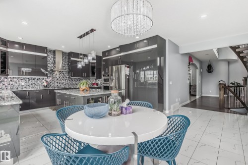 Modern kitchen featuring dark cabinetry, stainless steel appliances, a mosaic tile backsplash, and a central island with countertop seating - 4104 8 Street Nw, Edmonton, AB - Indoor Photo Showing Dining Room