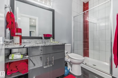 Bathroom featuring a contemporary gray vanity with a light-colored countertop, an oversized mirror, a glass-enclosed shower with white and red wall tiling, and dark floor tiling - 4104 8 Street Nw, Edmonton, AB - Indoor Photo Showing Bathroom