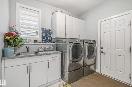 Dedicated laundry area featuring a utility sink, light-toned countertop, white cabinetry with silver hardware, and a window for natural light - 4104 8 Street Nw, Edmonton, AB - Indoor Photo Showing Laundry Room