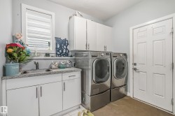 Dedicated laundry area featuring a utility sink, light-toned countertop, white cabinetry with silver hardware, and a window for natural light - 