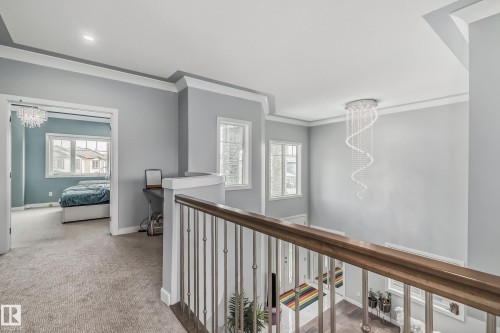 Upper landing featuring a decorative crystal chandelier, light gray wall tones, crown molding, and a wood handrail with metal balusters - 4104 8 Street Nw, Edmonton, AB - Indoor Photo Showing Other Room