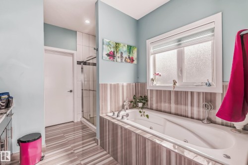 Bathroom featuring a white soaking tub with deck-mounted fixtures, complemented by striped wall tiling - 4104 8 Street Nw, Edmonton, AB - Indoor Photo Showing Bathroom