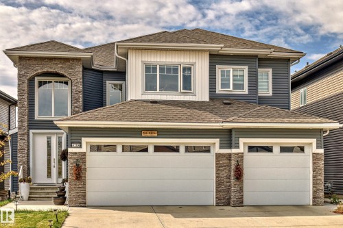 Multi-level residence featuring a two-car garage with transom windows, a stone accent facade, and a prominent arched window on the upper level - 4104 8 Street Nw, Edmonton, AB - Outdoor With Facade