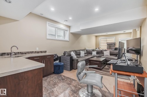 Lower-level living area featuring a built-in wet bar with a single basin sink, wood-finish cabinetry, and mosaic tile backsplash - 4104 8 Street Nw, Edmonton, AB - Indoor