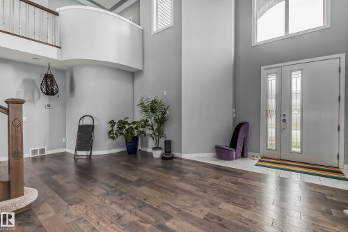 Two-story entry featuring wood-finish flooring, a double-door entryway with decorative glass inserts, and a second-story curved overlook with a wood railing - 4104 8 Street Nw, Edmonton, AB - Indoor Photo Showing Other Room