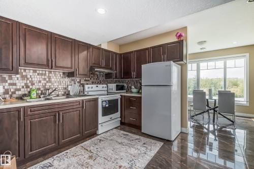 Kitchen featuring dark wood cabinetry, a mosaic tile backsplash, and white appliances - 4104 8 Street Nw, Edmonton, AB - Indoor Photo Showing Kitchen With Double Sink