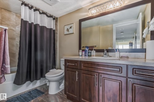 Bathroom featuring a spacious vanity with dark wood-finish cabinetry, a large framed mirror, and a crystal-accented light fixture - 4104 8 Street Nw, Edmonton, AB - Indoor Photo Showing Bathroom