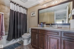 Bathroom featuring a spacious vanity with dark wood-finish cabinetry, a large framed mirror, and a crystal-accented light fixture - 
