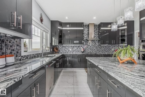 Modern kitchen featuring high-gloss charcoal cabinetry, speckled granite countertops, a mosaic tile backsplash, stainless steel appliances, and a central island with pendant lighting - 4104 8 Street Nw, Edmonton, AB - Indoor Photo Showing Kitchen With Double Sink With Upgraded Kitchen