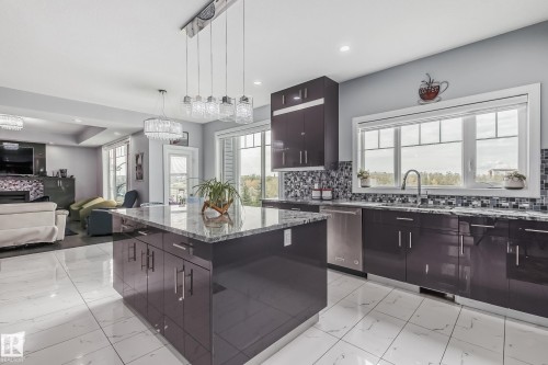Contemporary kitchen featuring a central island with a stone-look countertop, dark high-gloss cabinetry, stainless steel appliances, and a mosaic tile backsplash - 4104 8 Street Nw, Edmonton, AB - Indoor Photo Showing Kitchen With Upgraded Kitchen