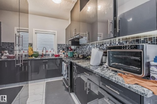 Contemporary kitchen with dark gray cabinetry, mosaic tile backsplash, and light-toned countertop - 4104 8 Street Nw, Edmonton, AB - Indoor Photo Showing Kitchen With Upgraded Kitchen