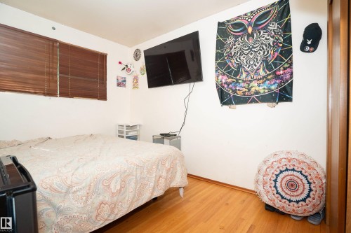 Interior room featuring a wall-mounted television, hardwood flooring, and a window with horizontal blinds - 5307 105 Street Nw, Edmonton, AB - Indoor Photo Showing Bedroom