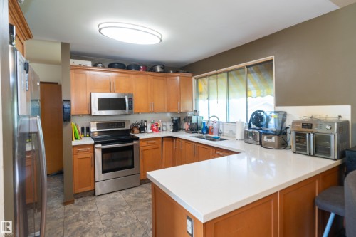 U-shaped kitchen featuring wood-finish cabinetry, white solid-surface countertops, and stainless steel appliances including a range with oven and an over-the-range microwave - 5307 105 Street Nw, Edmonton, AB - Indoor Photo Showing Kitchen With Double Sink