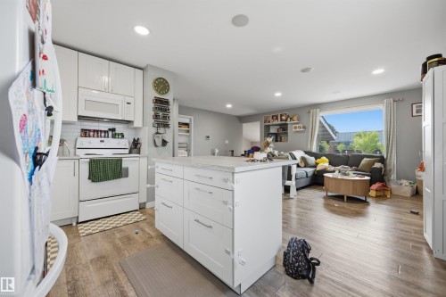 Open-concept interior featuring a white kitchen with an island, wood-finish flooring, white appliances, and recessed lighting - 4810 55 Avenue, Beaumont, AB - Indoor Photo Showing Kitchen