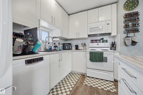 Kitchen featuring white shaker-style cabinetry, wood-finish flooring, white subway tile backsplash, white appliances, and light-toned countertops - 4810 55 Avenue, Beaumont, AB - Indoor Photo Showing Kitchen