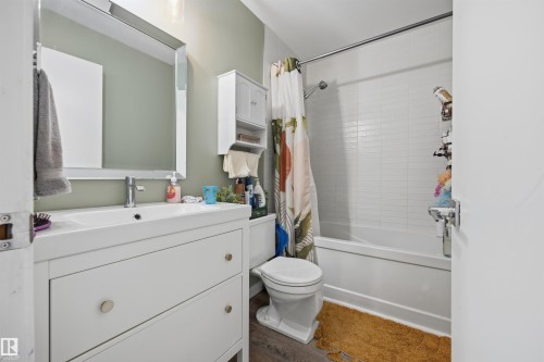 Bathroom featuring a white vanity with integrated sink, rectangular framed mirror, light green painted walls, white subway tile shower surround, and wood-finish flooring - 4810 55 Avenue, Beaumont, AB - Indoor Photo Showing Bathroom