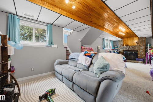 Lower level recreation space featuring a stone-clad fireplace with a black metal insert, a wood-paneled ceiling section, and recessed lighting - 4810 55 Avenue, Beaumont, AB - Indoor With Fireplace