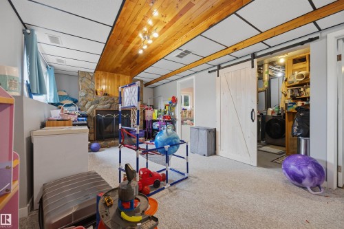 Basement featuring a stone fireplace with a black insert, wood-finish ceiling panels, light gray walls, light-toned carpet flooring, and a sliding barn door - 4810 55 Avenue, Beaumont, AB - Indoor Photo Showing Other Room
