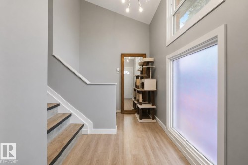 Foyer featuring wood-finish flooring, a contemporary staircase with dark risers, vaulted ceilings, and a large frosted window - 4810 55 Avenue, Beaumont, AB - Indoor Photo Showing Other Room