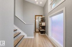 Foyer featuring wood-finish flooring, a contemporary staircase with dark risers, vaulted ceilings, and a large frosted window - 