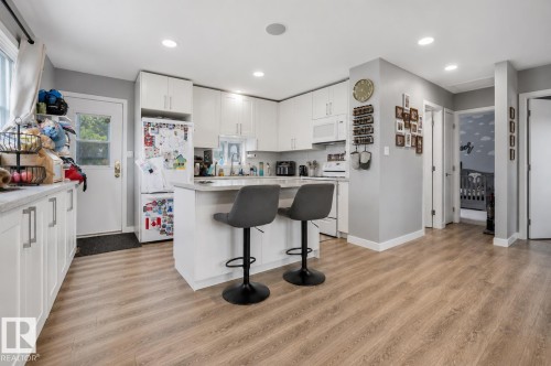 Kitchen featuring wood-finish flooring, white cabinetry, integrated appliances, and a central island with countertop seating - 4810 55 Avenue, Beaumont, AB - Indoor Photo Showing Kitchen