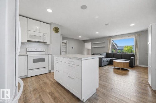 Kitchen featuring white cabinetry, white appliances, a white subway tile backsplash, and a central island with a light-toned countertop - 4810 55 Avenue, Beaumont, AB - Indoor Photo Showing Kitchen